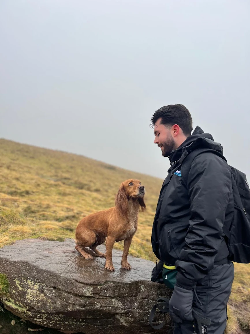 Joe, TopDog owner, standing outdoors by a stream with a dog